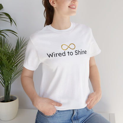 Person wearing a white t-shirt with 'Wired to Shine' text and infinity symbol, standing indoors.