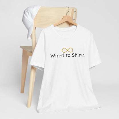 White t-shirt with 'Wired to Shine' text and logo on a wooden chair against a white background