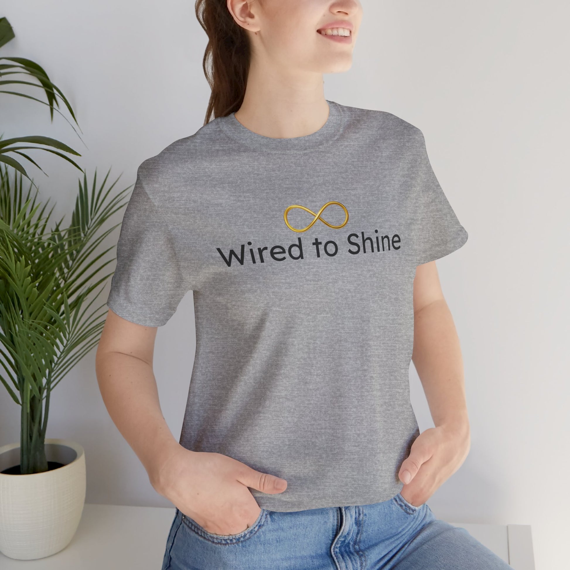 Person wearing a gray t-shirt with 'Wired to Shine' text and infinity symbol, standing indoors.