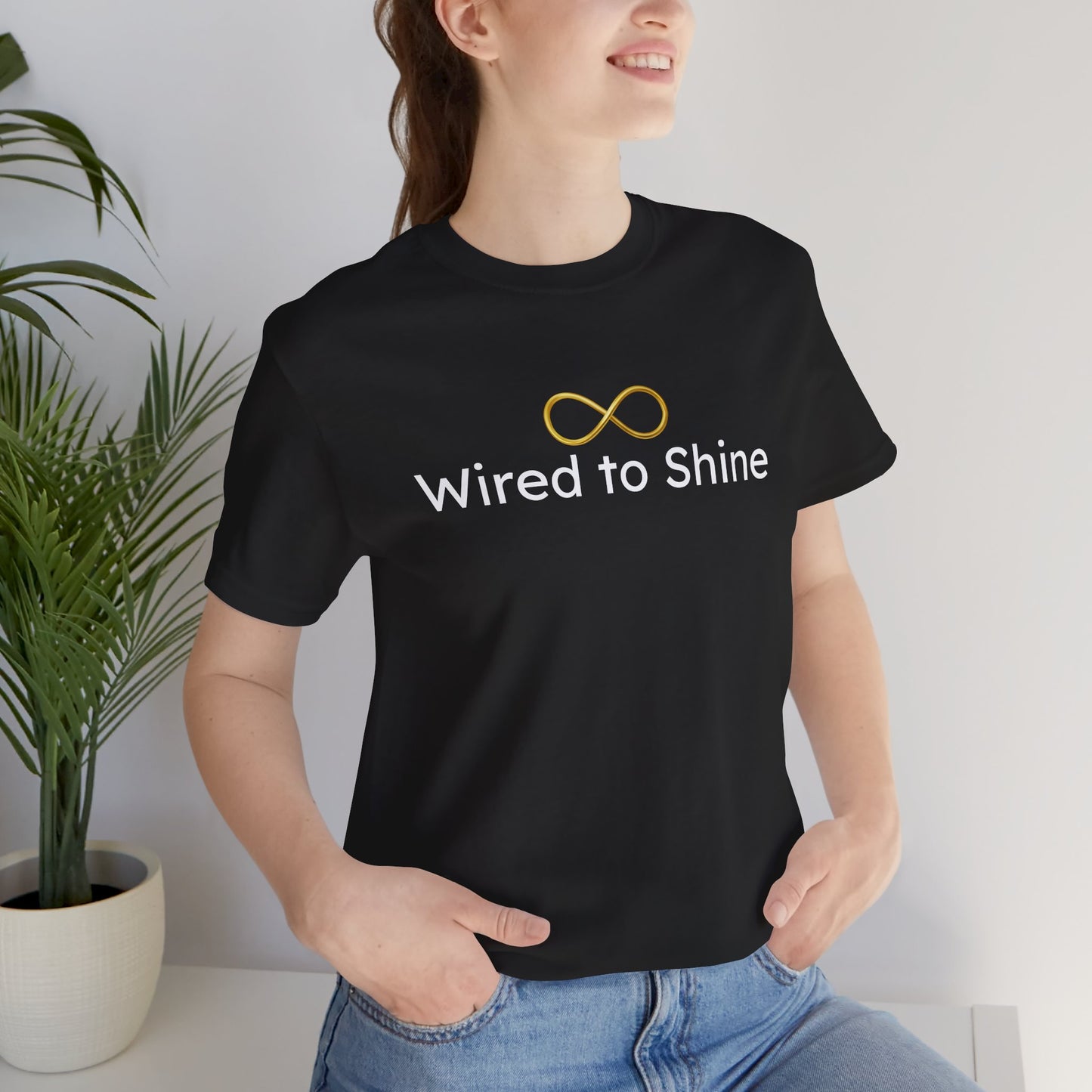 Person wearing a black t-shirt with 'Wired to Shine' text and infinity symbol, standing indoors.